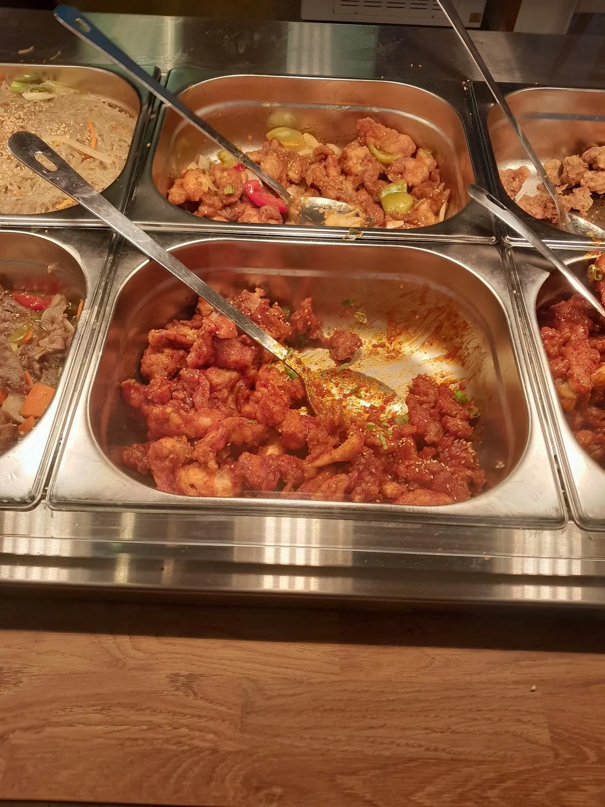The hot counter, steel trays of fried chicken, saucy chicken and noodles with serving spoons
